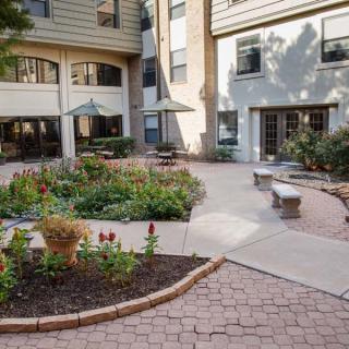 A serene courtyard with landscaped gardens, benches, and a paved walkway surrounded by a multi-story building.