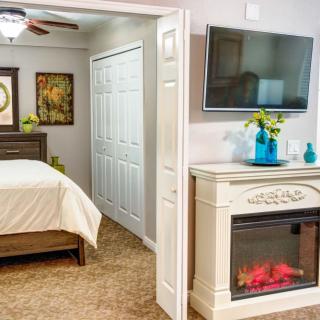 A cozy bedroom featuring a mounted television, electric fireplace, and elegant decor.