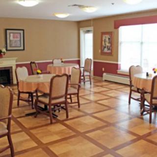 A cozy dining room with neatly arranged tables and chairs, featuring a wooden floor and soft lighting.