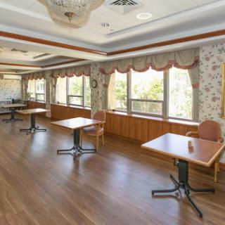 An empty restaurant interior featuring tables arranged near large windows, allowing for natural light to fill the space.