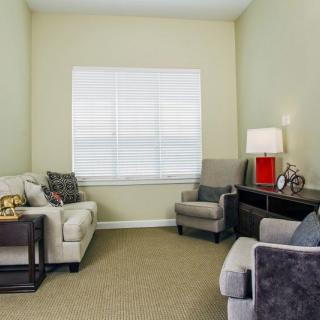 A cozy living room with sofas, armchairs, and a lamp by the window.