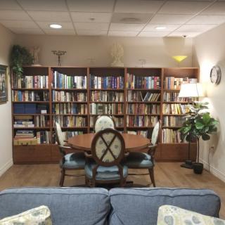 A cozy reading room with a large bookshelf, a table with chairs, and decorative plants.