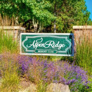 A scenic entrance sign for Aspen Ridge surrounded by lush greenery and colorful plants.
