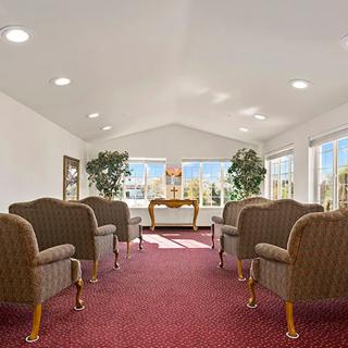 A well-lit waiting room with arranged chairs and a desk, featuring large windows and indoor plants.