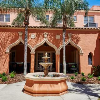A Mediterranean-style building with ornate arches and a central fountain in the courtyard, surrounded by palm trees.