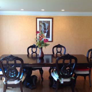 A well-appointed dining room featuring a dark wooden table with six chairs, a vase with flowers at the center, and a painting on the wall.
