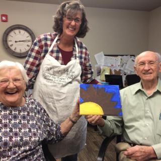 A joyful group of seniors displaying a painting during an art class.
