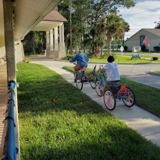 Two people riding bicycles down a sidewalk in a neighborhood setting.