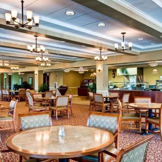A spacious dining area with elegant chandeliers, featuring neatly arranged tables and chairs on a carpeted floor.