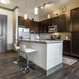 A modern kitchen interior featuring an island with seating, dark cabinets, and stainless steel appliances.