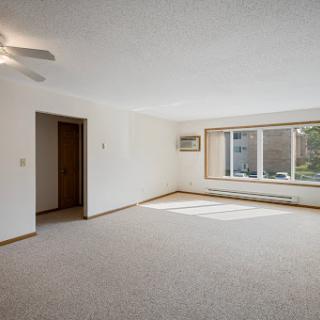 A spacious and bright vacant living room featuring a ceiling fan and large windows.