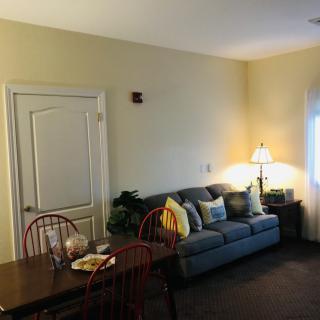 A cozy living room with a grey sofa, colorful cushions, and a small dining table.