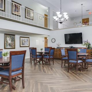 A spacious and elegant dining area featuring wooden tables and chairs, a large chandelier, and a wall-mounted television.