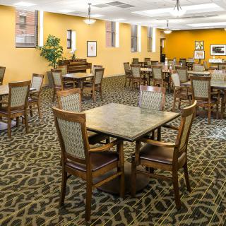 A spacious dining area with neatly arranged tables and chairs, featuring a patterned carpet and a warm color palette.