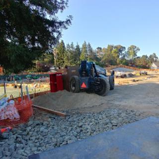 A tractor working on a construction site, surrounded by gravel and equipment under a clear blue sky.