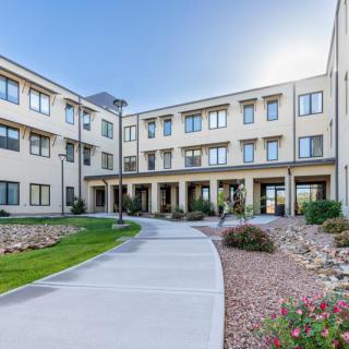 A modern three-story building with a landscaped courtyard and paved pathway.