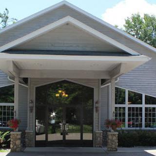 A front view of a building entrance with a pitched roof and large windows.