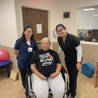 A patient in a wheelchair poses with two healthcare professionals during a rehabilitation session.
