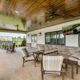 A spacious and modern outdoor patio featuring comfortable seating and a ceiling fan, offering a relaxing garden view.