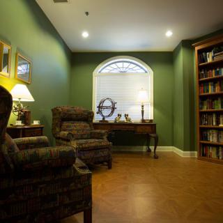 A cozy living room with green walls, featuring armchairs and bookshelves.