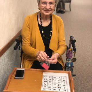 An elderly woman smiling while playing bingo indoors.