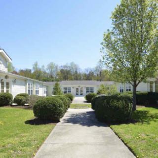 A scenic view of a white building surrounded by trees and bushes under a clear blue sky.