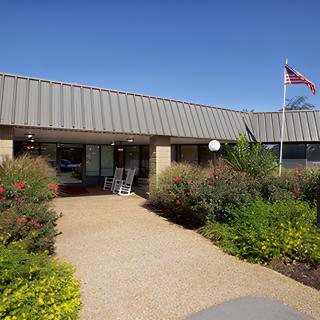 A building entrance with a landscaped garden and flag on a clear day.