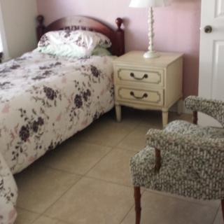 A cozy bedroom with a single bed featuring floral bedding, a nightstand with a lamp, and an armchair.
