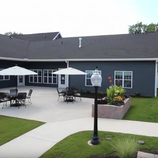 A patio area with outdoor seating and umbrellas next to a building, featuring well-maintained landscaping.