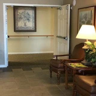 A cozy lounge area with two chairs, a table, and a lamp near an open doorway leading to a hallway.