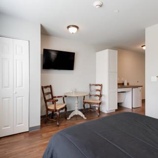 A cozy bedroom with a TV, seating area, and wood flooring.