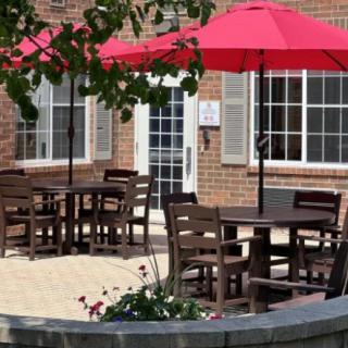An inviting patio with wooden tables and chairs shaded by red umbrellas outside a brick building.