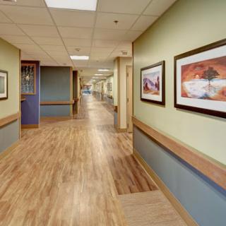 A well-lit interior hallway featuring artwork on the walls and wooden flooring.