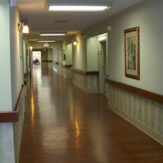 An empty hallway in a nursing home with wooden floors and paintings on the walls.