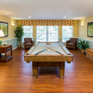 A cozy game room featuring a pool table, comfortable seating, and warm wooden flooring.