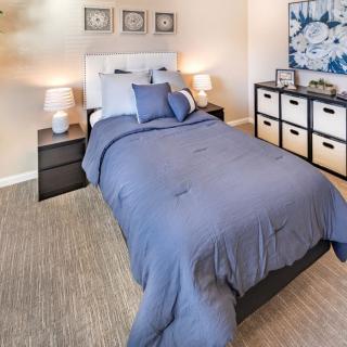 A cozy bedroom with a neatly made bed, bedside lamps, and organized storage.