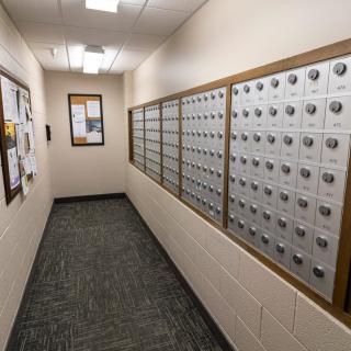 A hallway lined with multiple mailboxes and a community bulletin board on the wall.