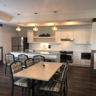 A modern kitchen with white cabinets, an island counter, and a dining area featuring pendant lighting.