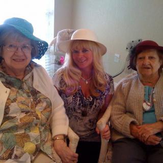 Three women wearing hats are sitting together and smiling indoors.