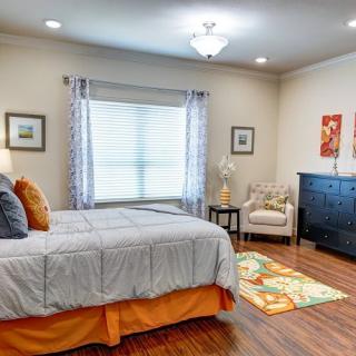 A modern and cozy bedroom featuring a neatly made bed with gray and orange accents, decorated with framed artwork and a comfortable armchair.