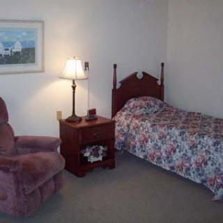 A cozy bedroom with a single bed, nightstand, lamp, and armchair in traditional decor.