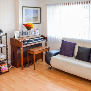 A cozy living room with a piano and a sofa, illuminated by natural light.