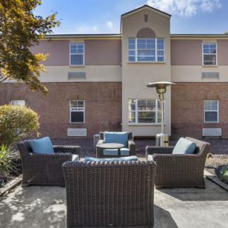 A cozy patio seating area with wicker furniture in front of a two-story building.