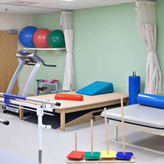 A well-equipped physical therapy room with a treadmill, exercise balls, and therapy tables.