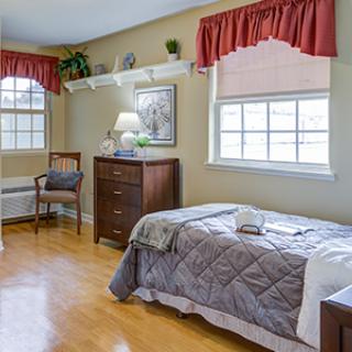 A cozy bedroom with a single bed, dresser, and natural light from two windows.