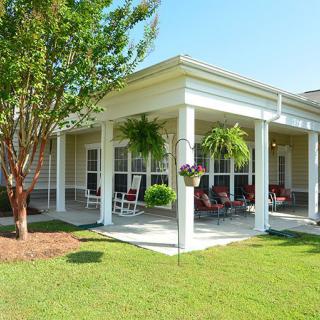 A cozy porch with outdoor seating surrounded by a well-maintained garden and trees.