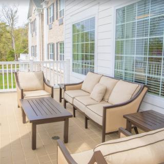 A cozy outdoor patio with cushioned seating and a coffee table, adjacent to a house with large windows.