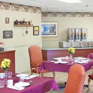 A neatly arranged dining room with tables set for guests, featuring decorated walls and a drinks dispenser in the background.