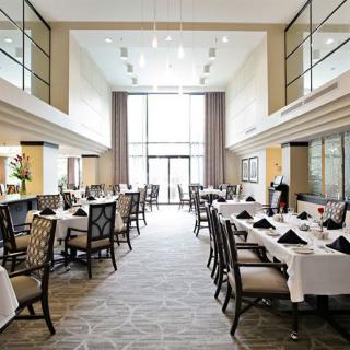 A spacious and elegant restaurant interior with tables set under white tablecloths and abundant natural light.