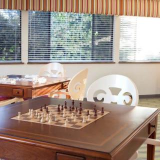 A cozy game room with a chessboard set up on a wooden table, illuminated by sunlight streaming through the windows.